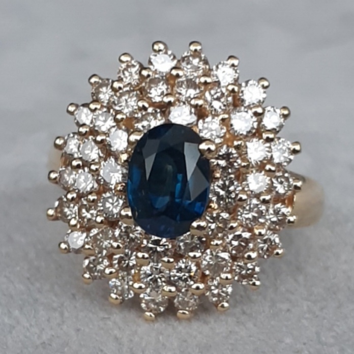 Bague marguerite en or 18K, saphir ovale et triple entourage de diamants, symbole absolu de l’élégance intemporelle, cette bague  conjugue la profondeur veloutée d’un saphir naturel à l’éclat céleste d’un triple halo de diamants. Héritière des codes classiques de la joaillerie, elle incarne l’harmonie parfaite des proportions et la beauté qui traverse les époques sans jamais se démoder.