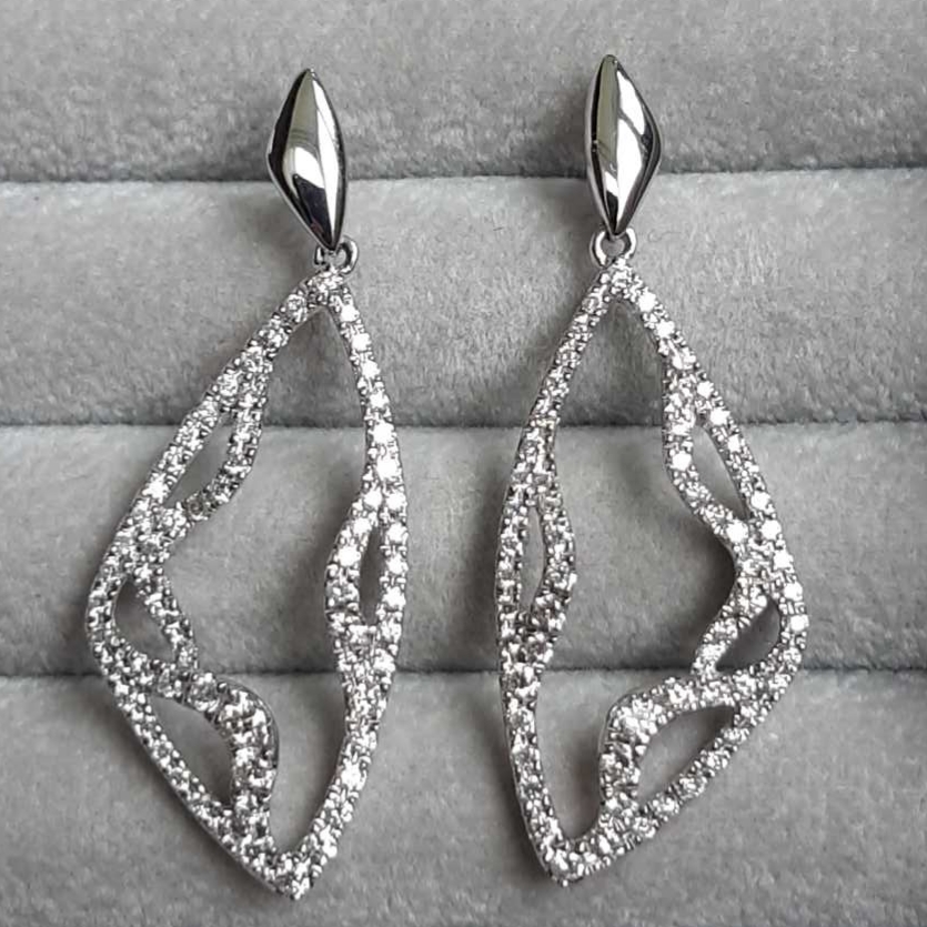 Boucles d’oreilles diamants – or blanc 18K, Lignes aériennes et éclat céleste : ces boucles d’oreilles jouent avec la lumière à chaque mouvement. Leurs courbes sculpturales transforment l’éclat des diamants en une poésie visuelle, alliant modernité et grâce intemporelle.